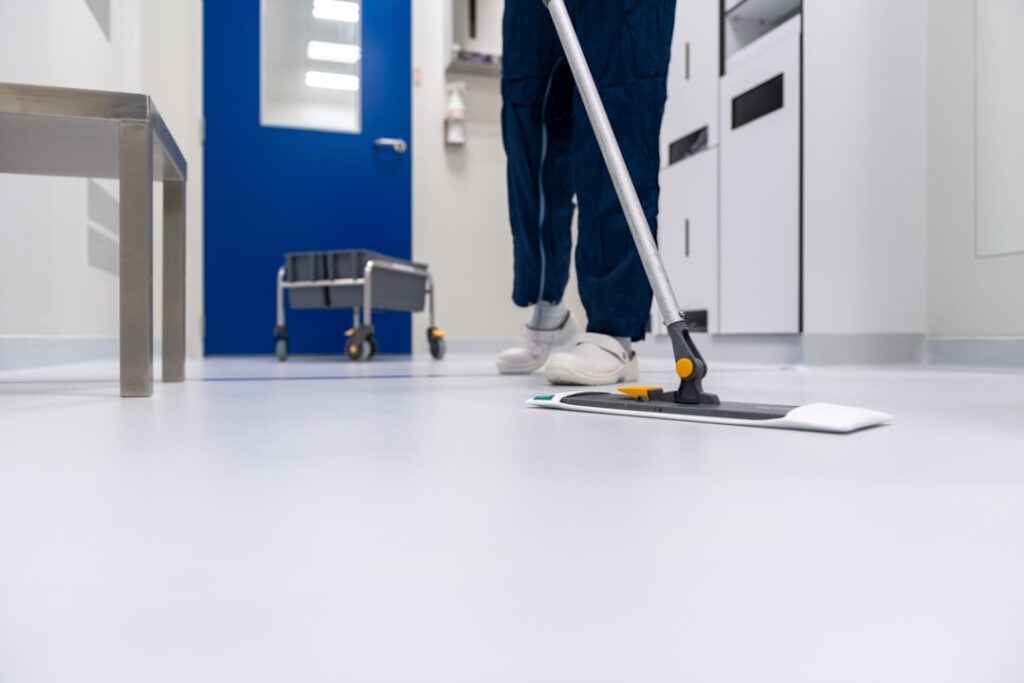 A healthcare worker in a clean uniform, holding a stain removal solution with a backdrop of a laundry setting.